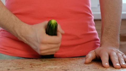 Man plays with a cucumber between his legs standing near the table. Cucumber closeup