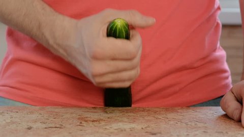 Man plays with a cucumber between his legs standing near the table. Cucumber closeup.
