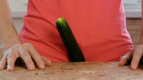 Man with a cucumber between his legs standing at the table. Cucumber closeup.