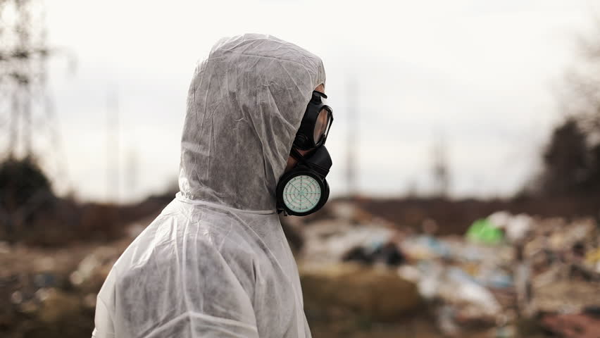 Virologist Man in Protective Costume and Respirator Gas Mask Walking near Landfill Site Pollution, Ecological Disaster