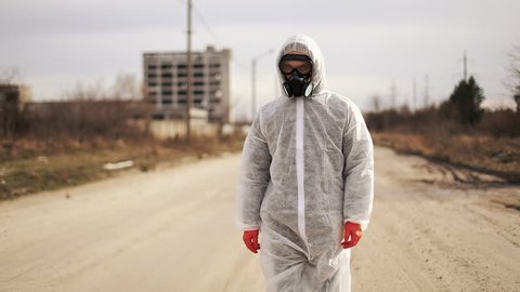 Virologist man in protective costume and respirator gas mask walk in a deserted city at the industrial factory background
