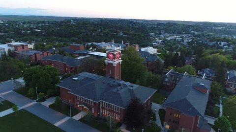 Aerial footage orbiting a university campus clock tower at sunset. 