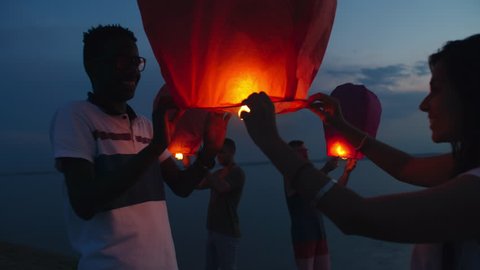 Medium shot of group of friends releasing sky lanterns on beach at dusk and celebrating something Adlı Stok Video