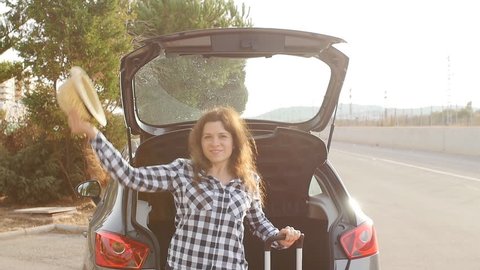 A young woman traveler with a suitcase stands near her car