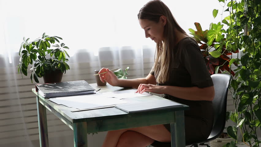 work at home. young beautiful freelancer woman is working at the table by the window in the house. modern ecological interior with living plants.