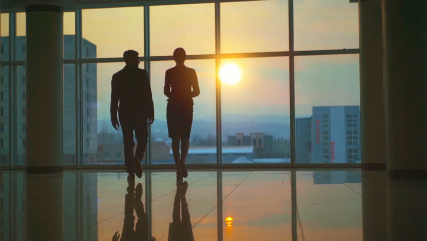 The man and woman walking in the office hall on a sunset background. slow motion