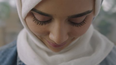 close up portrait of young muslim business woman looking up at camera confident wearing traditional hijab headscarf in office workspace background slow motion