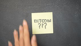 Closeup woman's hand sticking note with question Bitcoin??? on the blackboard - video in slow motion - Powered by Shutterstock - Get 15% off with code: PIKWIZARD15