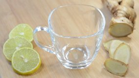 Pouring ginger lemon tea with fresh ginger and lemon slices on a wooden background.