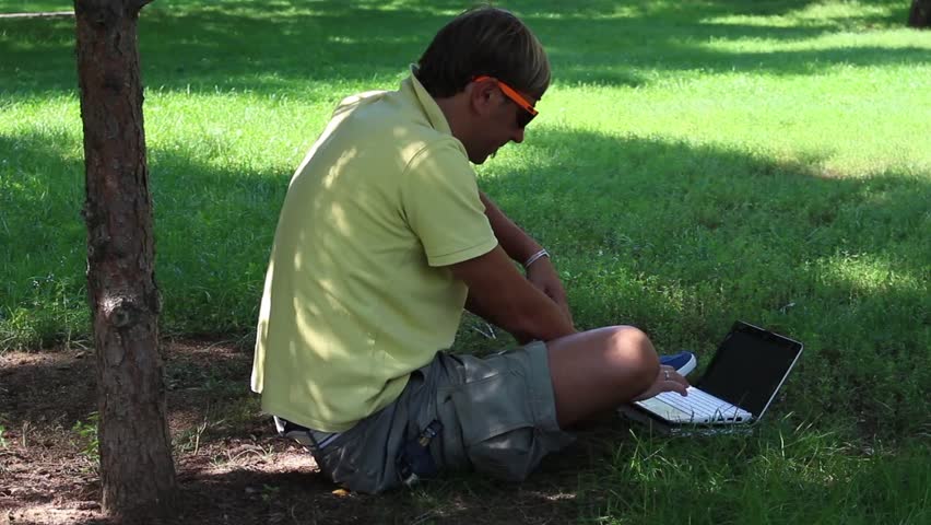 Man is using Laptop in a Park while chilling out and relaxing below the tree 1