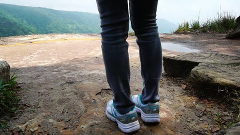Young traveling with jeans and sneaker walking to the top of the mountain cliff to looking beautiful view of tropical forest and sky and clouds on vacation. Asian woman travel alone.