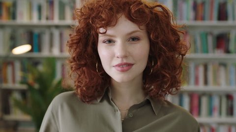 portrait of lovely young librarian woman standing in library attractive student smiling close up red head