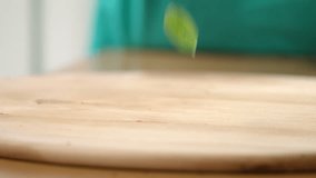 Green basil leaves being scattered across a chopping board by hand in kitchen in slow motion in 4K, macro extreme close up.