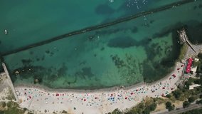 Beautiful beach in Odessa in Ukraine. On it there are many multicolored umbrellas with deckchairs and beach mats. Relaxing tourists are sunbathing and swimming in the sea. Aerial video recording.