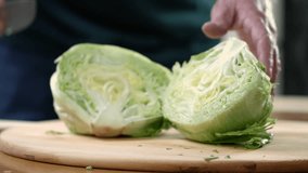 Green lettuce being chopped into pieces with a chef’s knife on a chopping board by hand in kitchen in slow motion in 4K, macro extreme close up.