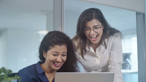 Two young and beautiful office female employees women working together on a laptop in a new start up office space on a project. Office girls are smiling and jubilant after executing important task