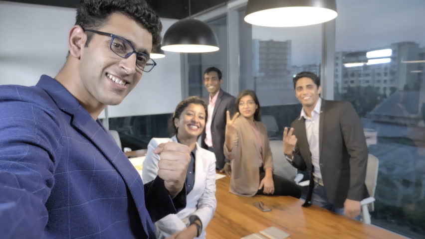 A happy and cheerful businessman taking a selfie with his business associates on a cellphone. A young delighted male team leader taking a selfie on a mobile phone with his efficient team in a office | Shutterstock HD Video #1009576439