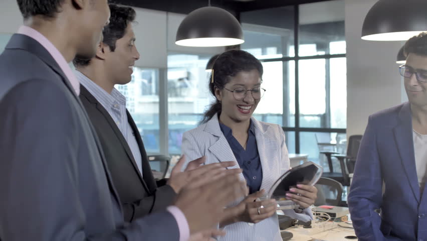 Mixed gender office colleagues smiling, applauding and congratulating a lady employee after winning an award. A group of male and female coworkers clapping and celebrating a success of a woman Royalty-Free Stock Footage #1009576811