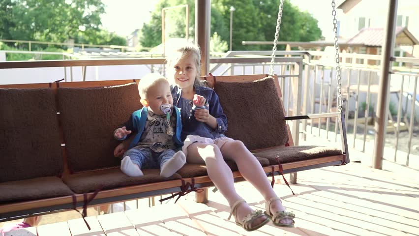 Children on the swing. The girl is sitting on a swing with a little boy. Brother and sister are sitting on the benches. The older sister hugs her younger brother on a wooden swing.