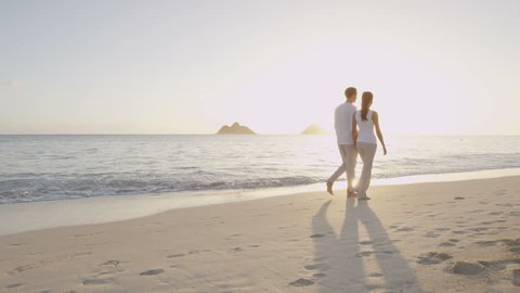 Honeymoon newlywed married young couple on beach walking in love holding hands at romantic sunrise' Multiracial woman and man relaxing on travel vacation holidays on Lanikai Beach, Oahu, Hawaii, USA