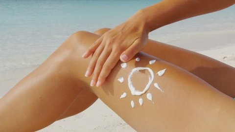 Beach woman applying sunscreen lotion on body - sun drawing skincare uv protection concept on sexy female bikini thigh leg closeup. Suntan person on Caribbean tropical vacation.