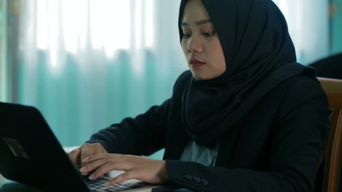 Southeast asian hijab business woman in suit hard working using laptop at home with two kind of tones