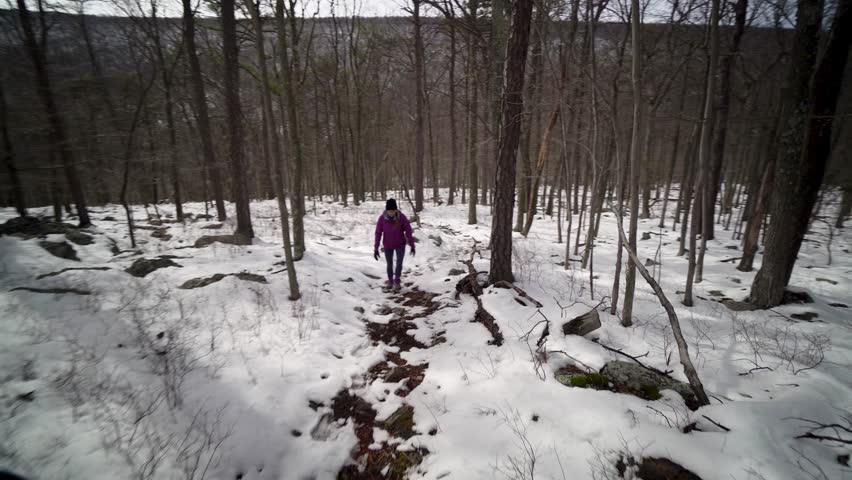 Steadicam in front of a pretty woman walking through a forest with snow.
