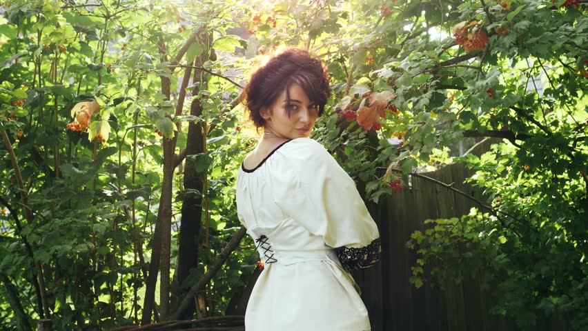 Cinemagraph - Ukrainian girl in sunrays posing on camera. A bouquet of statice in her hands and smiles at the camera. On her neck is a necklace of beads - gerdan.