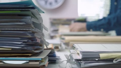 Employee working in the office with piles of files and paperwork, business administration and management concept