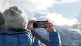 Young woman uses a smartphone to take a picture of beautiful view in the mountains, rear view
