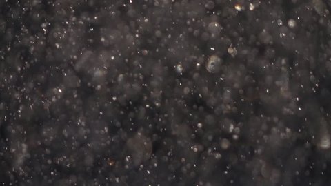 Sunny snowfall with shallow focus and sparkling colorful snowflakes on dark gray background. Abstract glittering backdrop in slow motion. Excellent meditative and relax intro with blinking gleams.