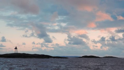 Great epic sky at dusk in Norway. Wonderful Nordic landscape, in background horizon and island. Orange or yellow sunlight penetrates through fluffy clouds. Lighthouse or observation deck on hill