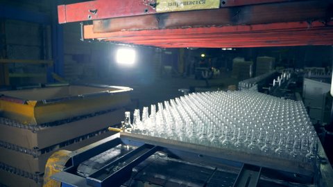 Fast motion footage of an industrial mechanism lifting a stack of bottles and relocating them