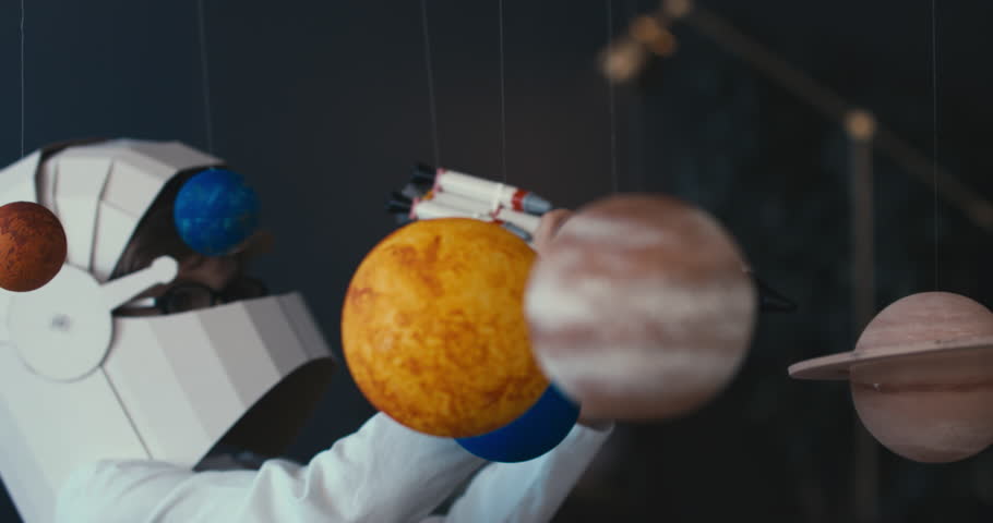 CU Cute little boy wearing cardboard astronaut helmet flying toy rocket through planets, exploring deep space. 4K UHD 60 FPS SLOW MO