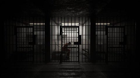 Depressed criminal sitting behind bars in old grunge prison cell.