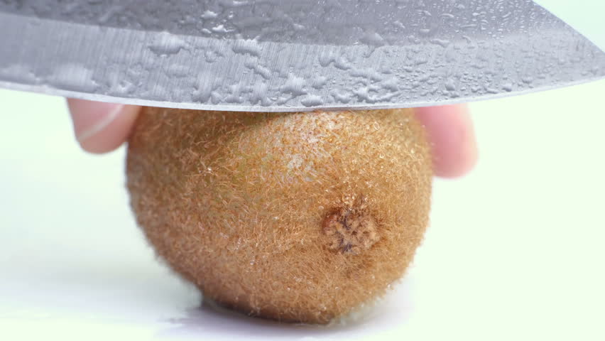 Kiwi being sliced in half on wet white background. Close up