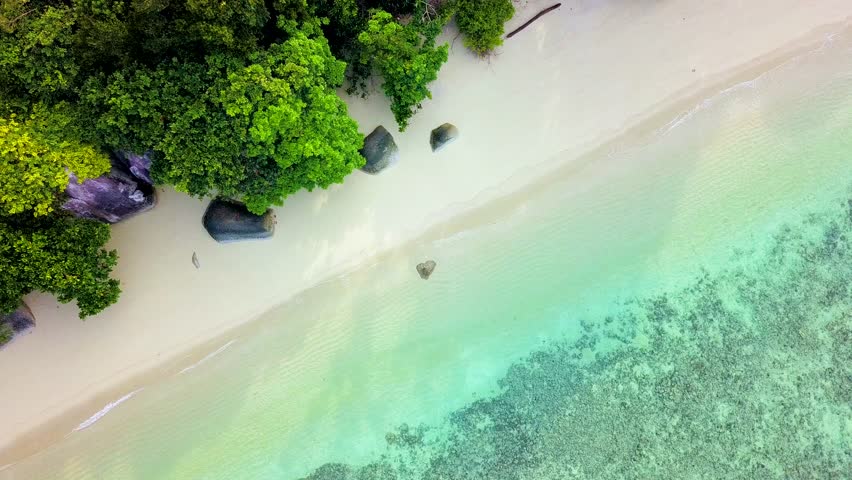 Fly up over a stony beach with azure green water. Stones in the water ...