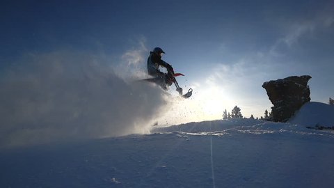 guy on a moto snowbike jumps and rides in the winter at sunset in the mountains
