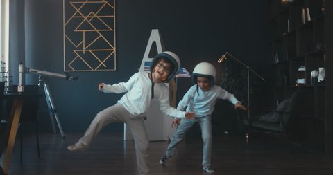 Cute little dreamer siblings boy and girl wearing space helmets pretending to be astronauts on Moon, getting out cardboard space rocket at home. 4K UHD 60 FPS SLOW MO