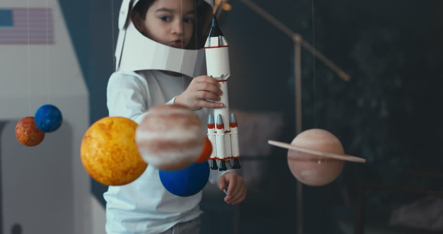 CU Little kid boy wearing cardboard astronaut helmet launching a toy rocket from a spaceport through planets. 4K UHD 60 FPS SLOW MO Royalty-Free Stock Footage #1009647971