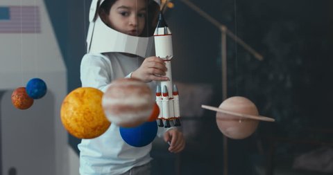 CU Little kid boy wearing cardboard astronaut helmet launching a toy rocket from a spaceport through planets. 4K UHD 60 FPS SLOW MO