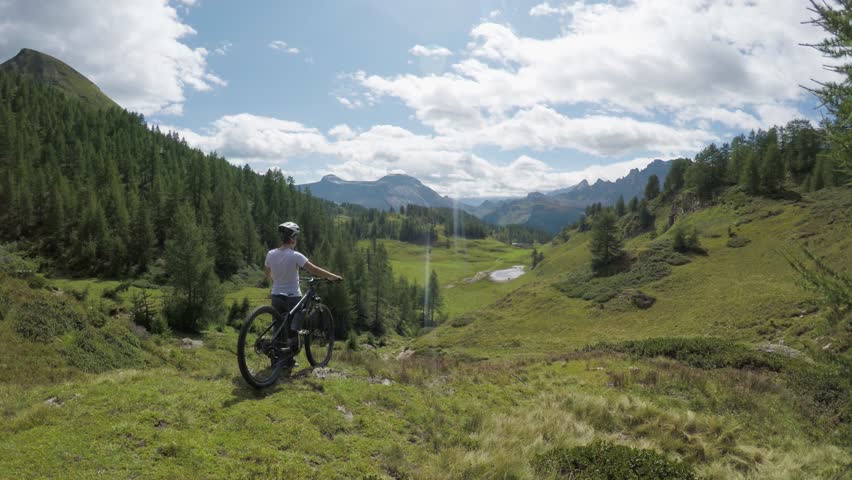 POV forward on hills and forest woods with mountain cyclist woman looking landscape panorama with mtb e-bike in summer outdoors.Wanderlust active sport travel people.Alps wild nature.4k drone video | Shutterstock HD Video #1009648412