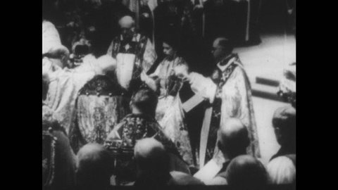 1950s: Man raises crown above Queen's head. Official places crown on Queen Elizabeth's head. Uniformed men and woman surround queen of England.