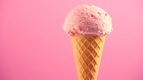Ice cream cone close-up. Icecream scoop in waffle cone rotated over pink background. Strawberry or raspberry flavor Sweet dessert closeup, rotation. 4K UHD video