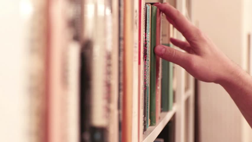 Hand reaches for and pulls classic book from library shelf; vintage look. Royalty-Free Stock Footage #1009667591