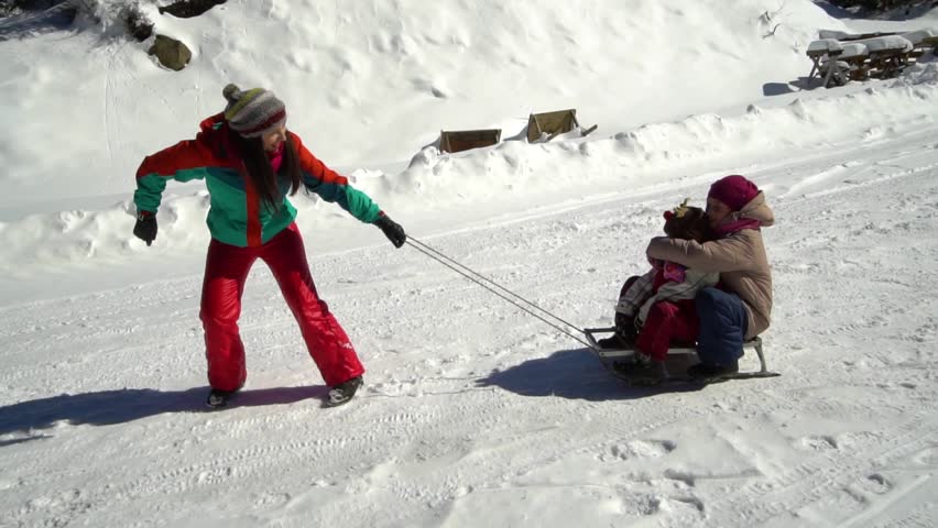 Happy family having fun playing in a snowy forest in the mountains in winter. Mom and her two children are sledding. They are laughing.