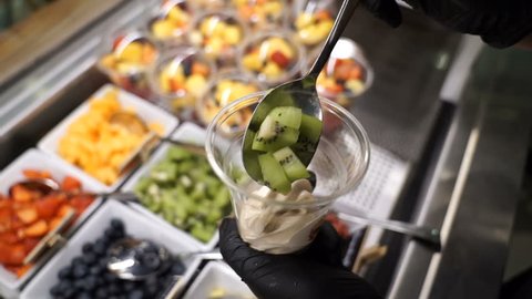 Kiwii being added to frozen yoghurt above fruity salad bar