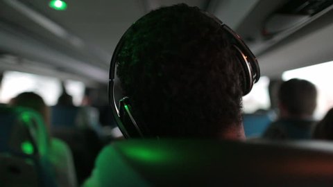 Person wears headphones listens to music while traveling by bus on road