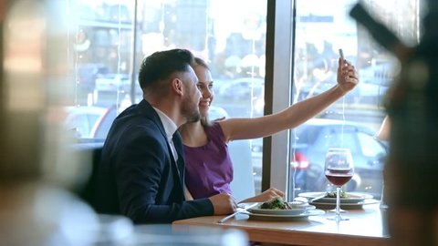 PAN of happy engaged couple smiling and taking selfie on romantic date in restaurant