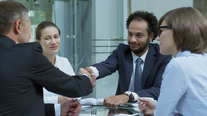 PAN shot of two experienced businessmen shaking hands and speaking with female colleagues at corporate meeting | Shutterstock HD Video #1009705013